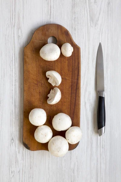 Champignon mushrooms on rustic wooden board over white wooden table, top view. From above, overhead.