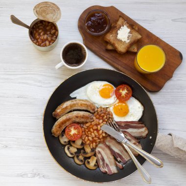 Tam İngiliz kahvaltısı bir tavada kızarmış yumurta, pastırma, sosis, fasulye ve üstten görünüm beyaz tahta masada tost ile. Düz yatıyordu. Yukarıda, ek yükü.