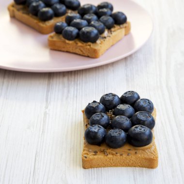 Fıstık ezmesi, yaban mersini ve beyaz ahşap bir masa yan görünüm üzerinde chia tohum ile Vegan tost. Sağlıklı kahvaltı. Seçici odak.