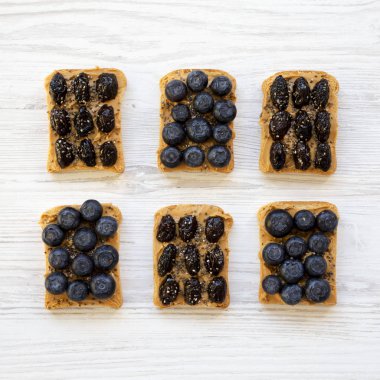 Fıstık ezmesi, yaban mersini, zeytin ve beyaz ahşap zemin, üstten görünüm üzerinde chia tohum ile Vegan tost. Sağlıklı beslenme. Yukarıdan, ek yük düz lay.