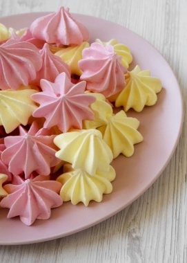 Beyaz ahşap zemin üzerinde pembe plaka üzerinde mini meringues yakın çekim.