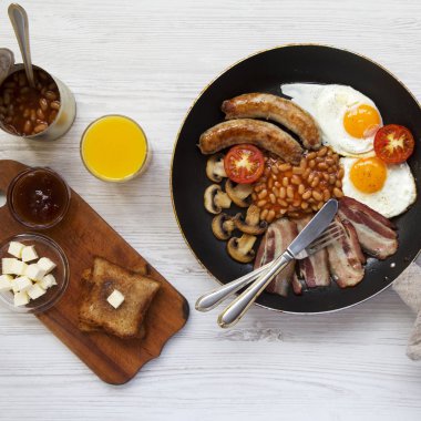 Bir tavada kızarmış yumurta, pastırma, sosis, fasulye ve tost beyaz tahta yüzeyi, havai görünümü ile İngiliz kahvaltısı. Düz yatıyordu. Yukarıdan.