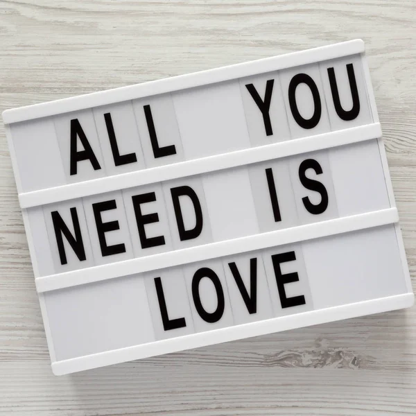 Lightbox with text 'All you need is love' over white wooden surface, top view. From above, flat lay, overhead.