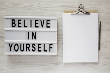 Metin 'Believe kendinizi', modern yönetim kurulu Pano ile kağıt beyaz ahşap zemin, üstten görünüm üzerinde. Yukarıdan, ek yükü yat. 