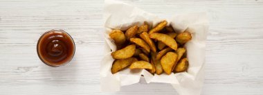 Üstten görünüm, kızarmış patates dilimleri kağıt kutusu ve Barbekü soslu Beyaz ahşap zemin üzerinde. Yukarıda, ek yükü.