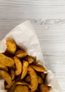 Beyaz ahşap bir masa kağıt kutusunda kızarmış patates dilimleri. Tepegöz, yukarıdan görünüm, top. 