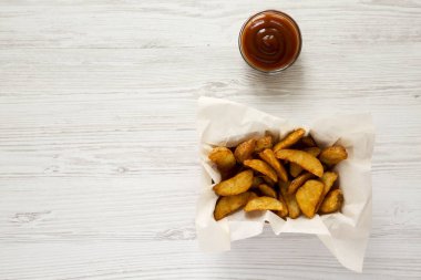 Yukarıdan, patates dilimleri bir beyaz tahta masada kağıt kutusu ve Barbekü soslu kızarmış. Tepegöz, üstten görünüm. Kopya alanı.