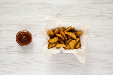 Kağıt kutusu ve barbekü sosu bir beyaz tahta yüzey üzerinde kızarmış patates dilimleri. Yukarıdan, tepegöz, görünümü top. Yakın çekim.