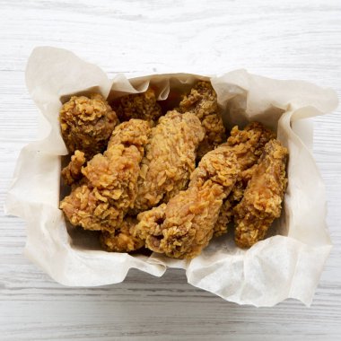 Kağıt kutusu beyaz ahşap zemin üzerinde kızarmış tavuk kanatları. Üstten görünüm, ek yükü. Yakın çekim.