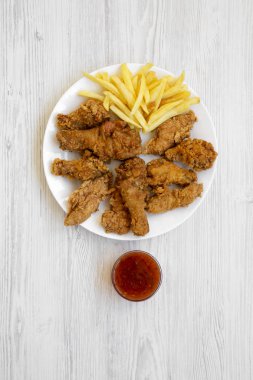 Lezzetli kızarmış tavuk budu, baharatlı kanatlar, patates kızartması, tavuk kanadı ve soslu Beyaz ahşap yüzey, en iyi görünümü üzerinde beyaz tabakta. Düz, Tepegöz, yukarıdan yatıyordu. 