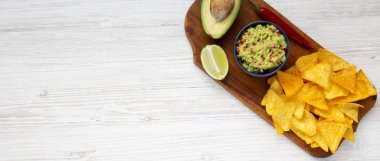 Guacamole Mısır Nacho, kireç, kesme yarı Beyaz ahşap yüzey üzerinde rustik ahşap tahta üzerinde avokado. Üstten Görünüm. Kopya alanı.