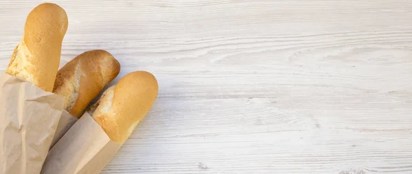 French baguettes in paper bags on white wooden surface, overhead