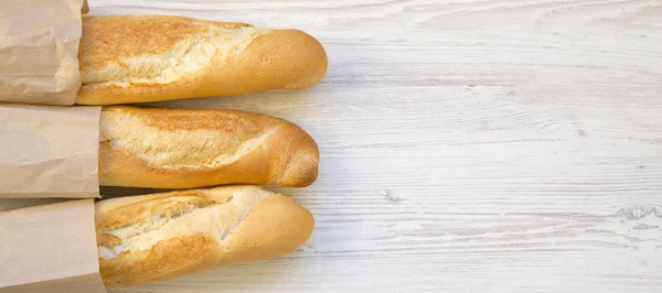 French baguettes in paper bags on white wooden background, top v — Stock Photo, Image