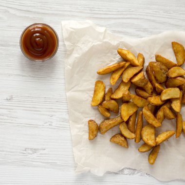 Kızarmış patates dilimleri bir beyaz tahta masada barbekü sosu ile.