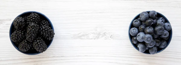 Olgun böğürtlen ve beyaz tahta üzerinde mavi kase yaban mersini — Stok fotoğraf