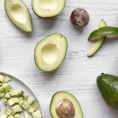 Beyaz ahşap yüzeyde bütün ve doğranmış avokado ek yükü vie