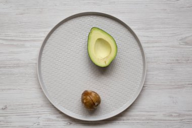 Beyaz ahşap yüzey üzerinde gri plaka üzerinde kemik yarım avokado, 