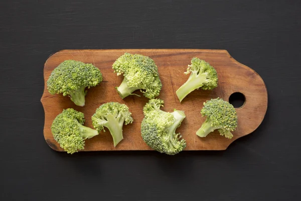 Çiğ brokoli adet siyah yüzeyinde, üst rustik ahşap tahta üzerinde — Stok fotoğraf