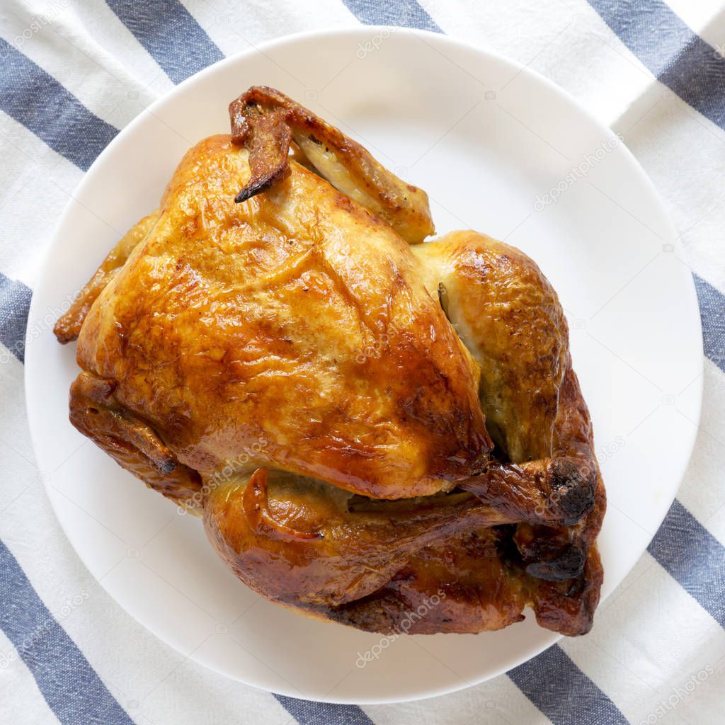 Homemade tasty rotisserie chicken on white plate, overhead view.