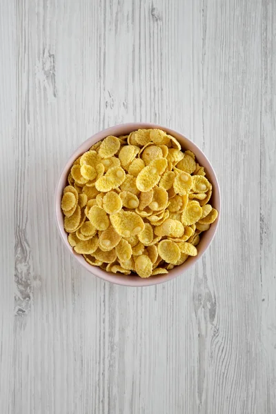 Corn flakes in a pink bowl for breakfast on a white wooden table