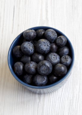 Beyaz ahşap zemin üzerinde mavi bir kase taze yaban mersini t