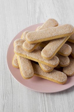 Savoyardi bisküvi Beyaz ahşap zemin üzerinde pembe plaka üzerinde l