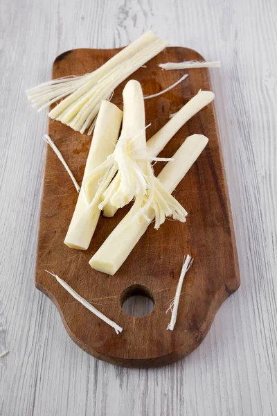 String cheese on rustic wooden board over white wooden surface,