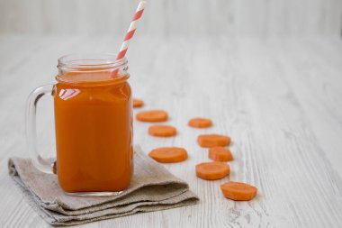 Cam sürahi havuç güler yüzlü beyaz ahşap yüzey, yan görünüm.