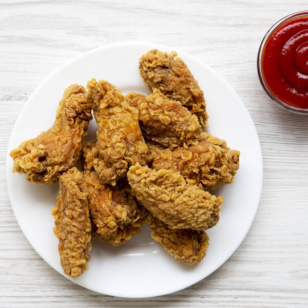 Куриные крылышки на круглой белой тарелке с кетчупом над белым вуу

