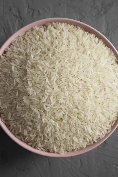 Dry white rice basmati in a pink bowl over gray surface, top vie — Stock Photo, Image