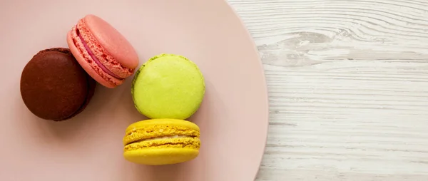 Macarons colorés sur une assiette rose sur fond de bois blanc , — Photo