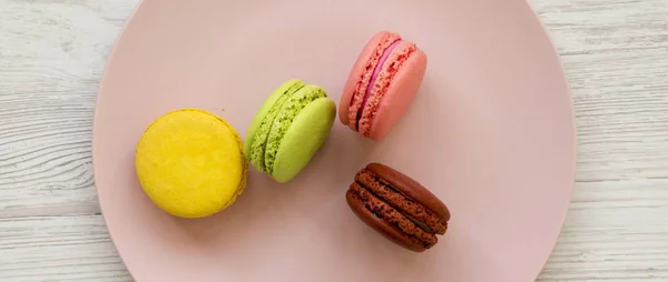 Macarons doux et colorés sur une assiette rose sur du su en bois blanc — Photo