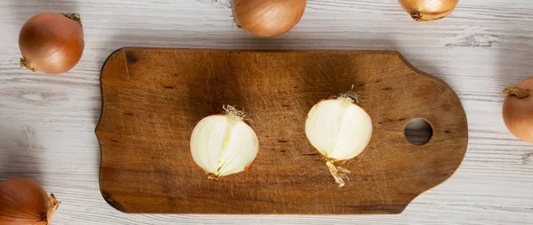 Unpeeled raw yellow onions on rustic wooden board over white woo