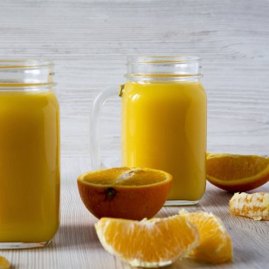Beyaz ahşap arka üzerinde cam kavanozlarda ev yapımı taze portakal suyu