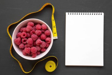 Pembe bir kase ham ahududu, boş not defteri ve ölçüm bandı