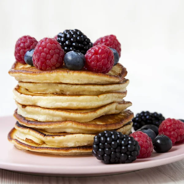 Beyaz ahşap yüzeyde pembe bir plaka üzerinde çilek ile pancake,