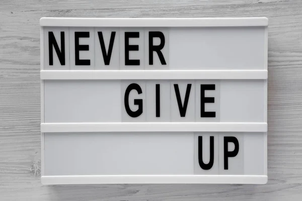 'Never give up' words on modern board over white wooden backgrou — Stock Photo, Image