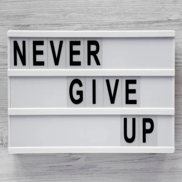 "Никогда не сдаваться" слова на современной доске по белой деревянной поверхности . — стоковое фото