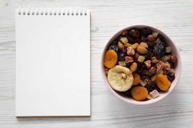 Kurutulmuş meyve ve fındık pembe bir kapta, beyaz w üzerinde boş not defteri
