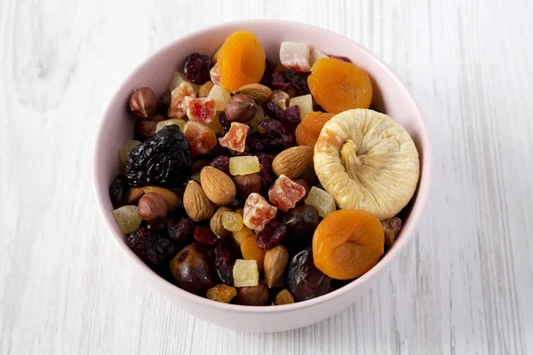 Beyaz ahşap yüzey üzerinde pembe bir kapta kurutulmuş meyve ve fındık, 