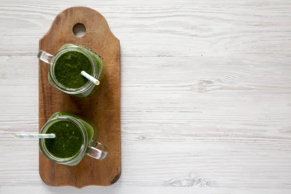 Smoothie verde em frascos de vidro em tábua de madeira rústica sobre w branco — Fotografia de Stock