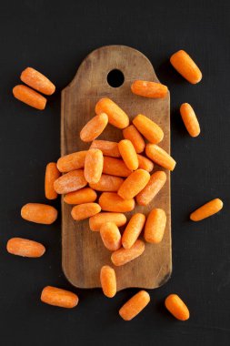 Siyah bir yüzey üzerinde rustik ahşap tahta üzerinde taze bebek havuç,