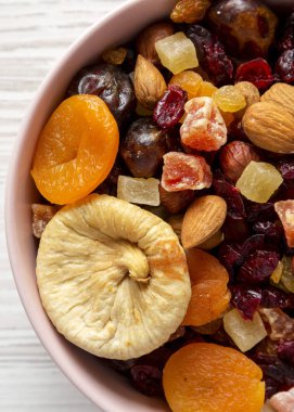 Beyaz ahşap yüzey üzerinde pembe bir kapta kurutulmuş meyve ve fındık, 