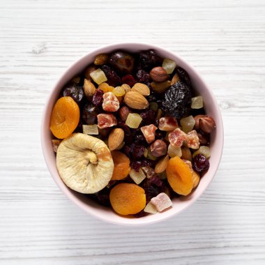 Beyaz ahşap yüzey üzerinde pembe bir kapta kurutulmuş meyve ve fındık. 