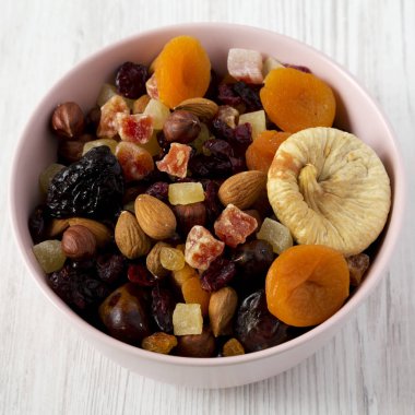 Beyaz ahşap backgroun üzerinde pembe bir kapta kurutulmuş meyve ve fındık