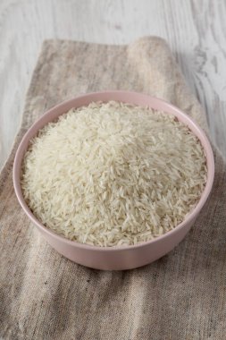 Beyaz ahşap backgrou üzerinde pembe bir kase kuru beyaz pirinç basmati