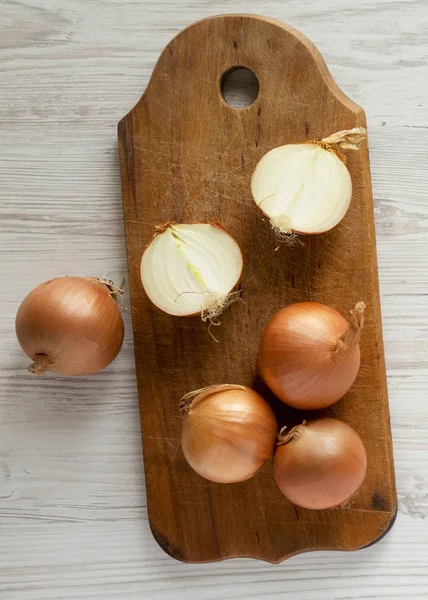 Unpeeled raw yellow onions on rustic wooden board over white woo — Stock Photo, Image