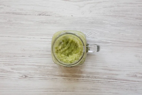 Top view, green celery smoothie in a glass jar over white wooden