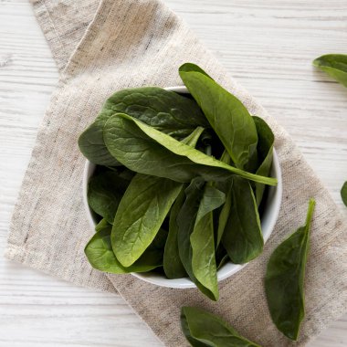 Beyaz ahşap yüzey üzerinde bir kapta taze çiğ ıspanak, üst görünümü.