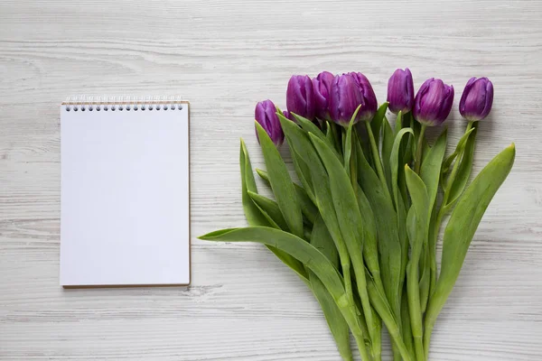 Purple tulips and blank notebook on a white wooden background. F